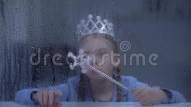 戴着<strong>魔法棒</strong>的戴着皇冠的小女孩独自坐在雨窗后